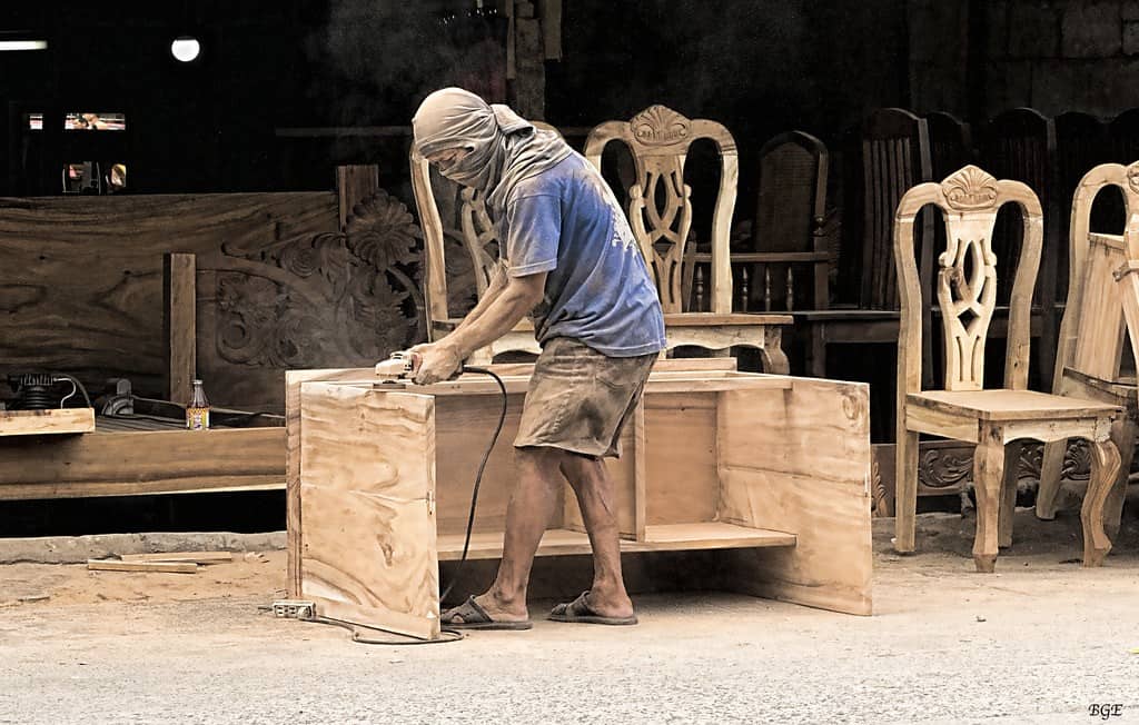 Een meubelmaker schuurt een houten meubelstuk.